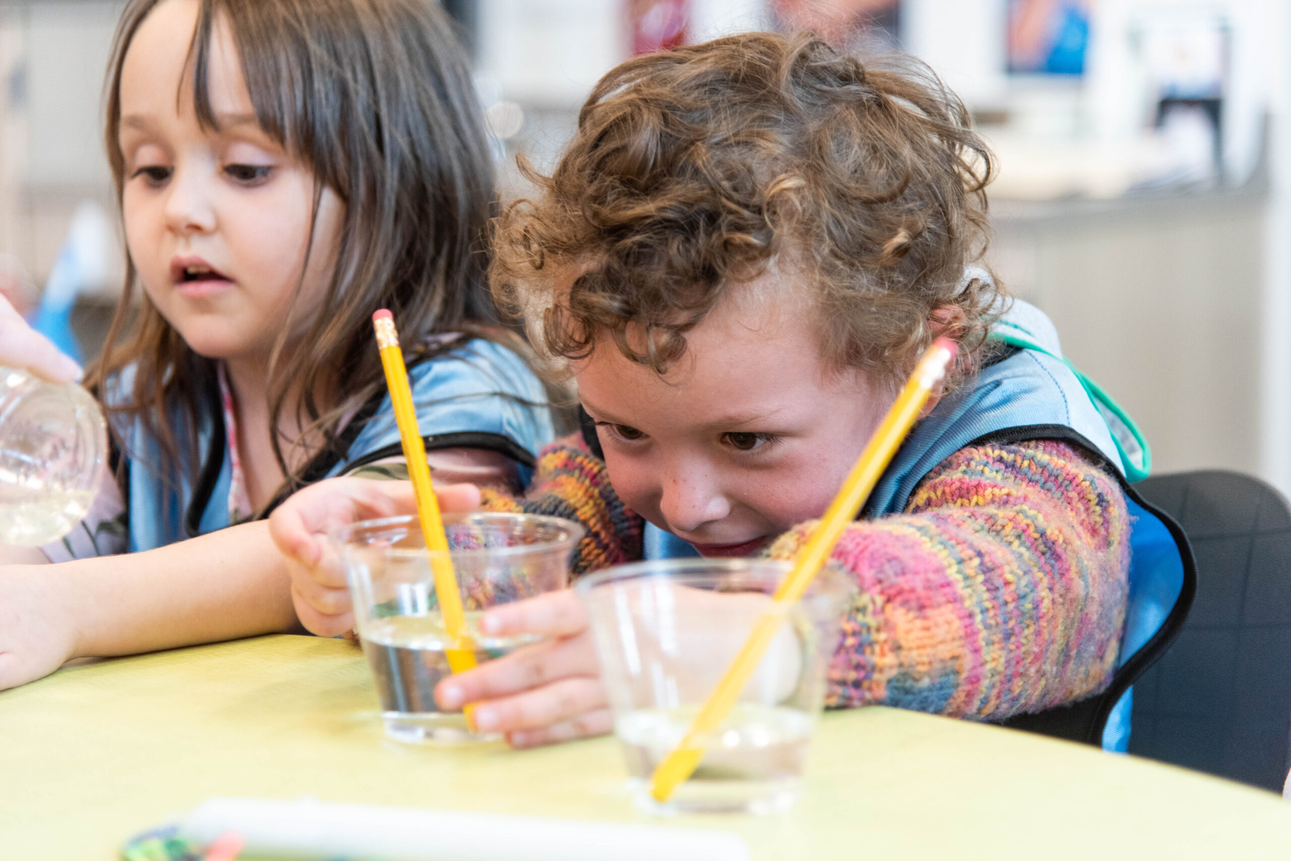 Alumna de preescolar durante un experimento científico con un vaso de agua y lápices